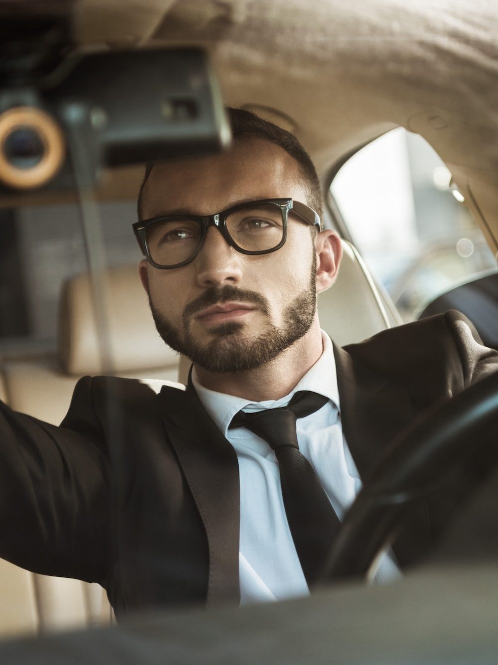 handsome driver in suit driving car and fixing mirror